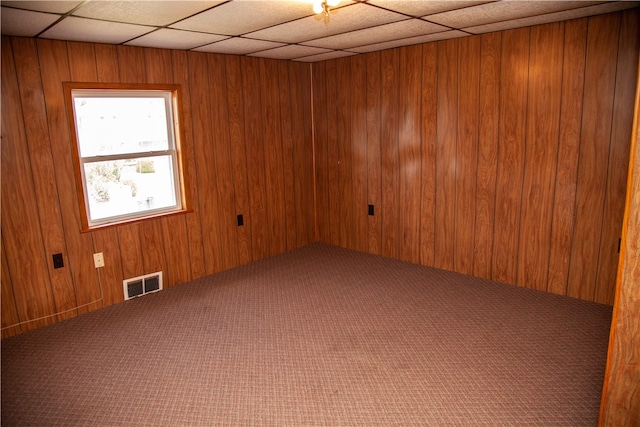 carpeted empty room with wood walls and a drop ceiling