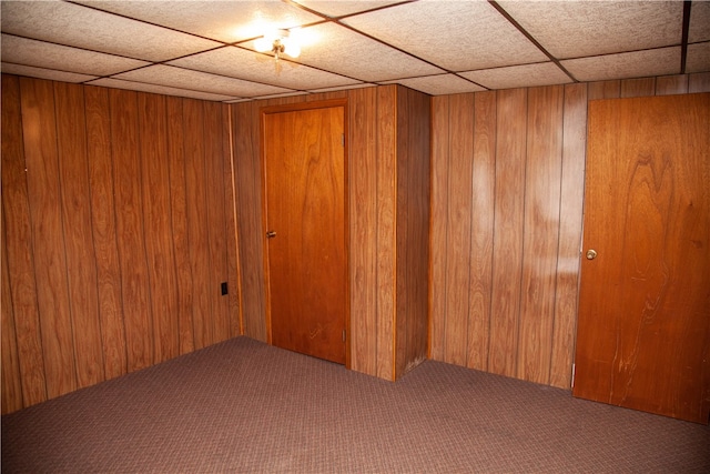 carpeted spare room with wooden walls and a drop ceiling