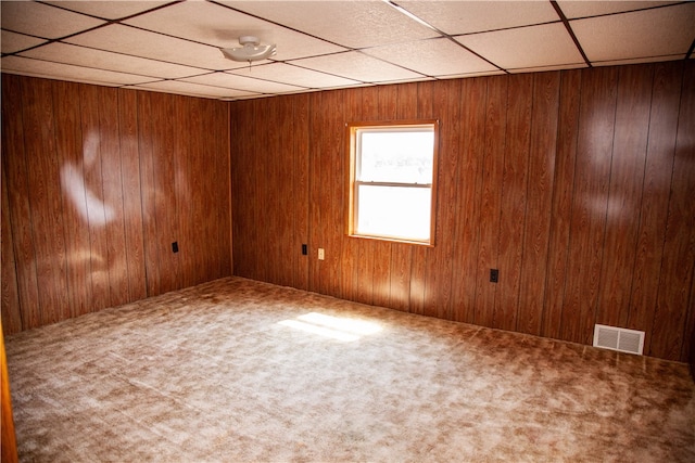 unfurnished room with wood walls, carpet, and a drop ceiling