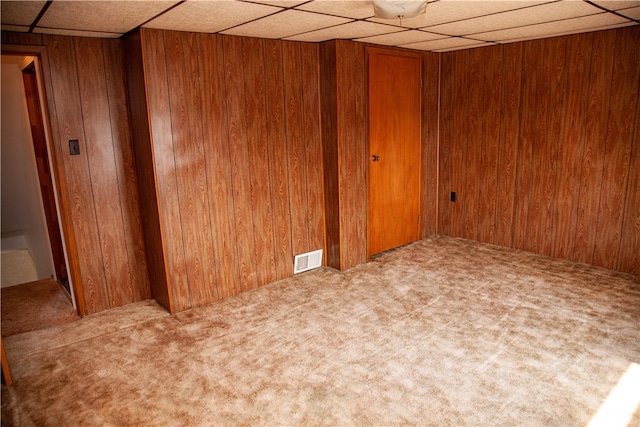 carpeted empty room with wooden walls and a drop ceiling