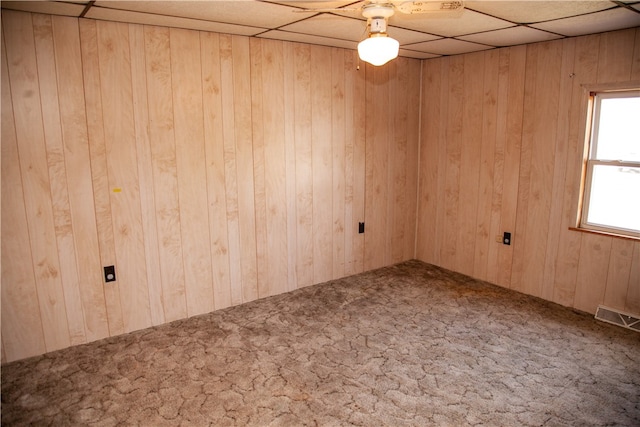 spare room with a drop ceiling, wooden walls, and carpet flooring