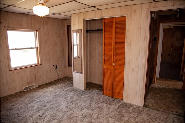 unfurnished bedroom featuring a paneled ceiling, a closet, carpet floors, and wooden walls