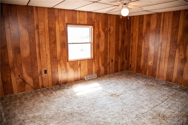 carpeted spare room with a paneled ceiling, ceiling fan, and wood walls