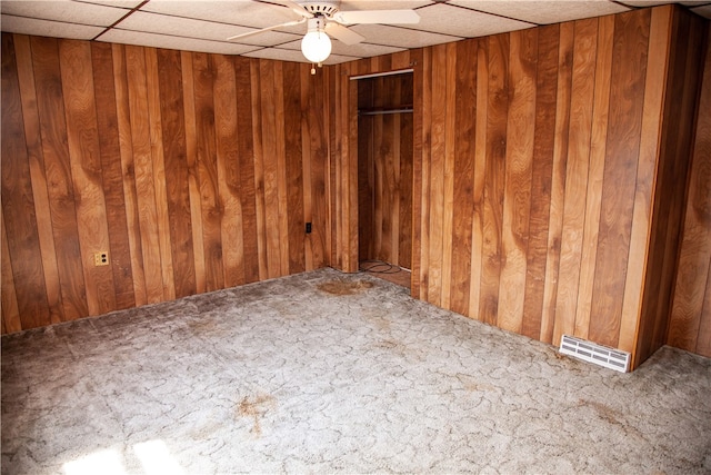 unfurnished room featuring wood walls, ceiling fan, and a drop ceiling