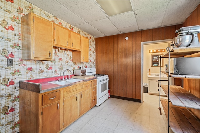 kitchen with wooden walls, white gas range oven, a paneled ceiling, light floors, and a sink