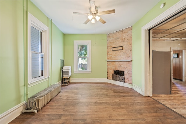 living area with a fireplace, radiator heating unit, a ceiling fan, wood finished floors, and baseboards