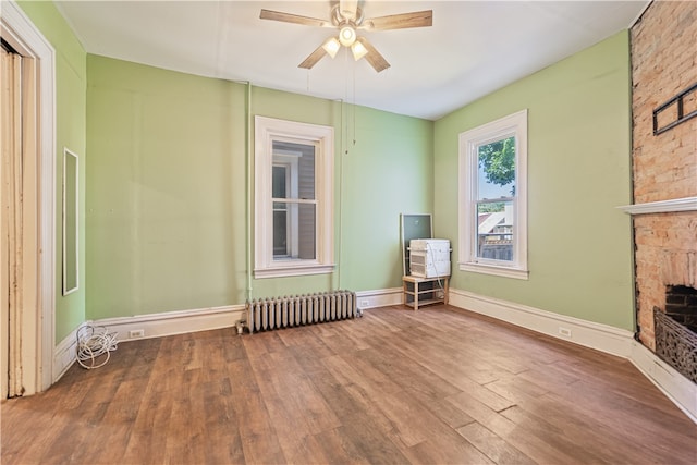 interior space with a stone fireplace, wood finished floors, a ceiling fan, baseboards, and radiator