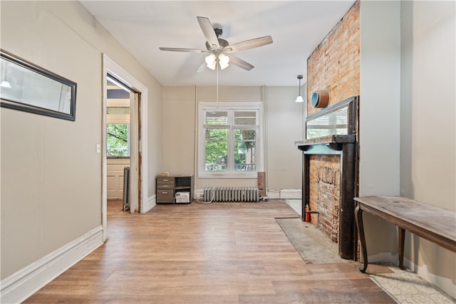 unfurnished living room featuring ceiling fan, a stone fireplace, radiator heating unit, and wood finished floors