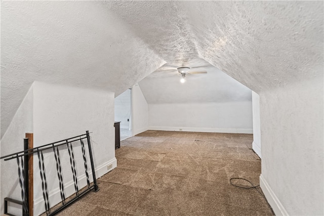 additional living space with a textured ceiling, a textured wall, lofted ceiling, baseboards, and carpet