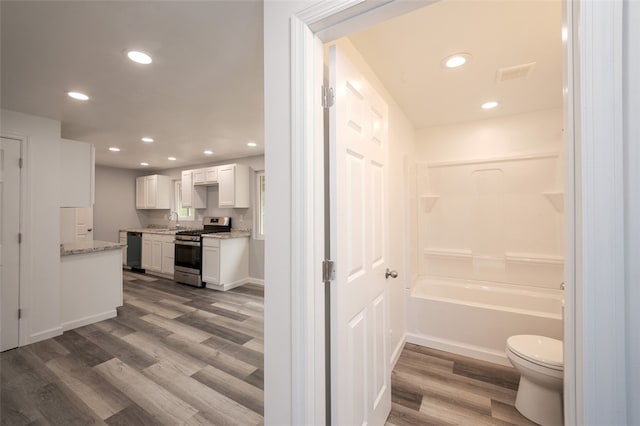 bathroom with a bathing tub, hardwood / wood-style floors, vanity, and toilet