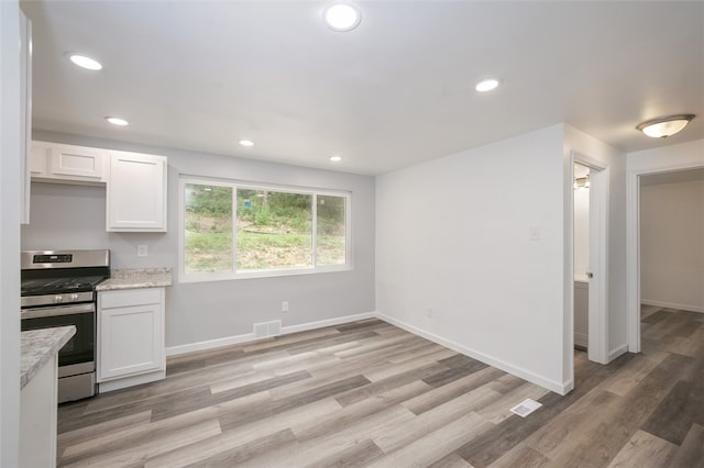 kitchen with light stone countertops, white cabinets, light hardwood / wood-style floors, and stainless steel range