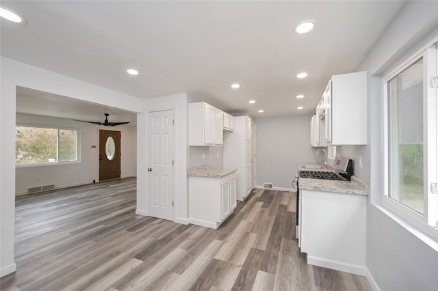 kitchen featuring light wood-type flooring, light stone counters, white gas range oven, white cabinetry, and ceiling fan