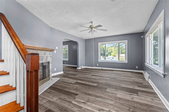 unfurnished living room featuring dark wood-type flooring, ceiling fan, a tiled fireplace, and a healthy amount of sunlight