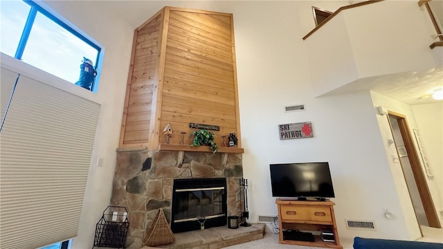 living room featuring a high ceiling, a stone fireplace, carpet floors, and wooden walls