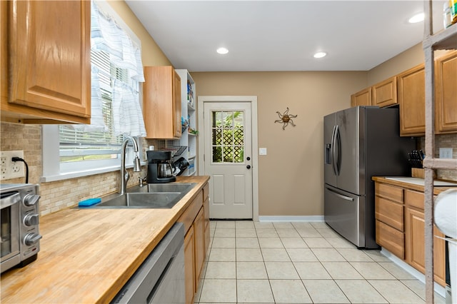 kitchen with light tile patterned floors, sink, stainless steel appliances, butcher block counters, and decorative backsplash