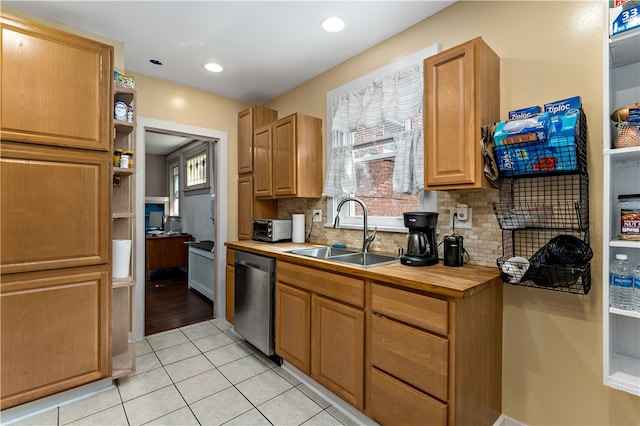 kitchen with sink, butcher block counters, backsplash, light tile patterned floors, and stainless steel dishwasher