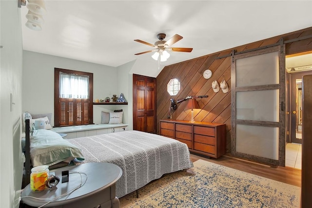 bedroom with light hardwood / wood-style floors, ceiling fan, and wood walls