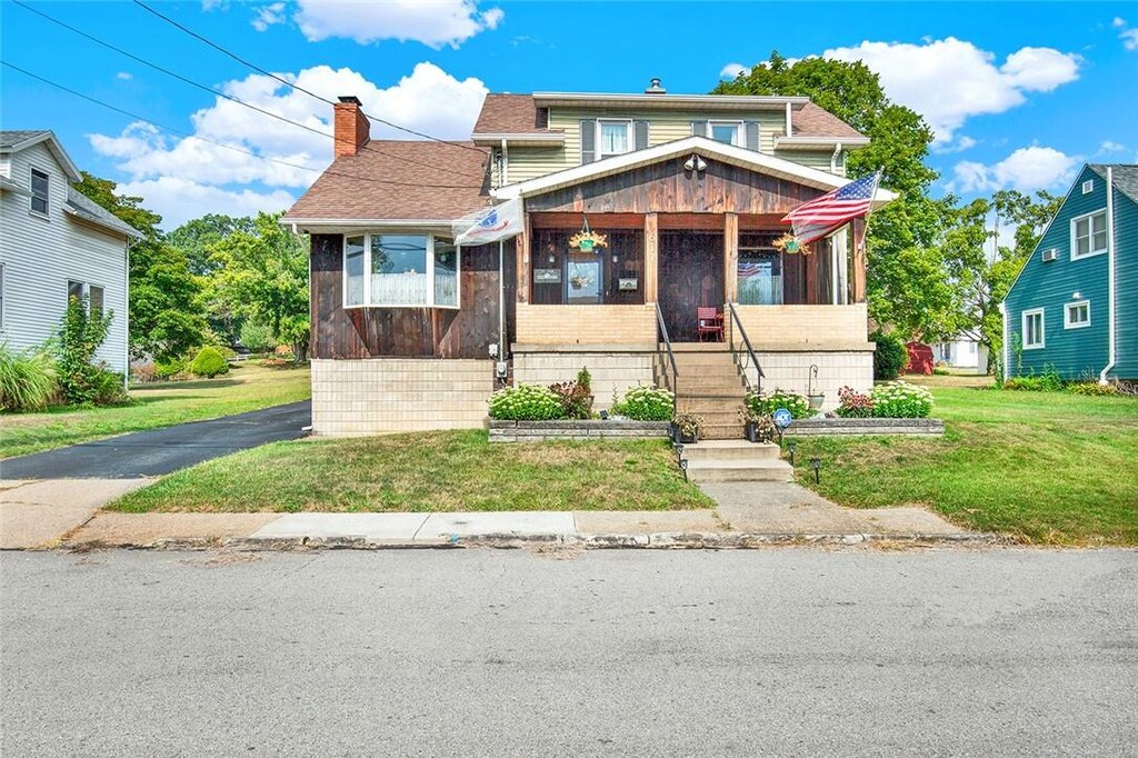 view of front of property featuring a chimney, roof with shingles, a front yard, and a sunroom
