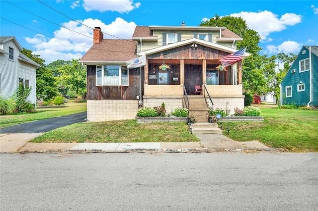 view of front of property featuring a chimney, roof with shingles, a front yard, and a sunroom