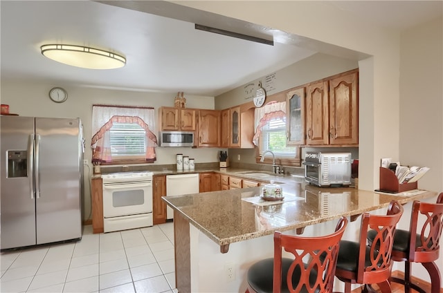 kitchen featuring a kitchen breakfast bar, light stone counters, kitchen peninsula, sink, and appliances with stainless steel finishes