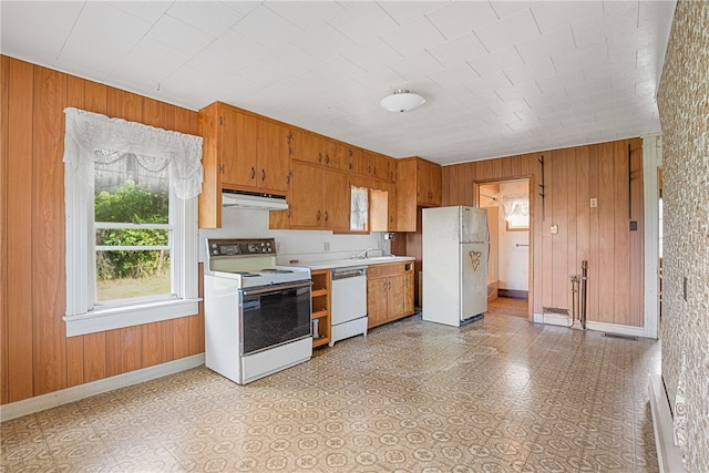 kitchen with wood walls, light tile patterned floors, white appliances, and sink