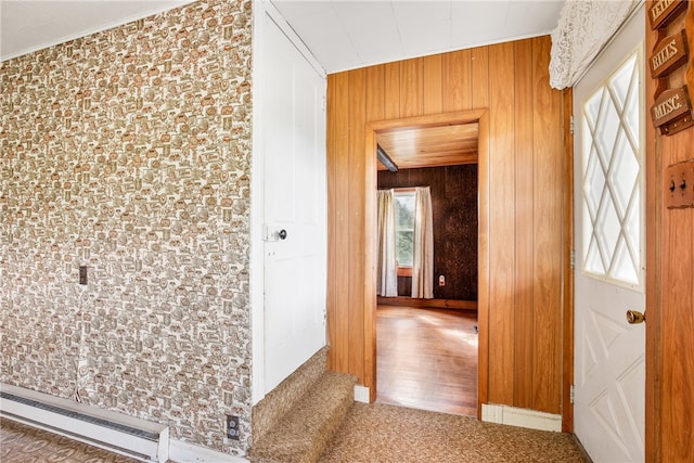 corridor with a baseboard heating unit, carpet flooring, and wooden walls