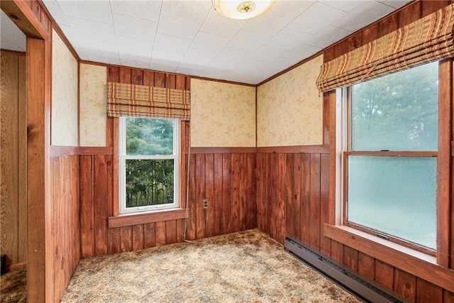 unfurnished room featuring a baseboard heating unit, carpet, and wood walls