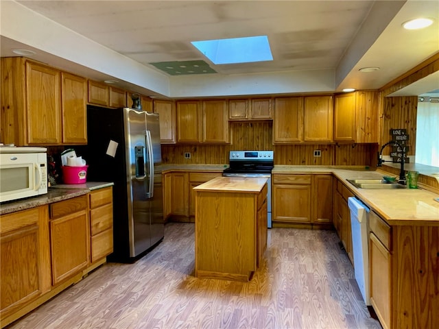 kitchen featuring a skylight, stainless steel appliances, a center island, sink, and light hardwood / wood-style floors