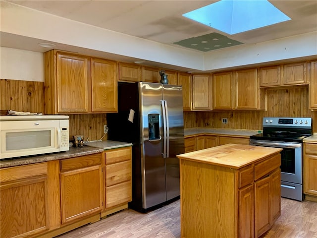 kitchen featuring a skylight, stainless steel appliances, wooden counters, a kitchen island, and light hardwood / wood-style floors