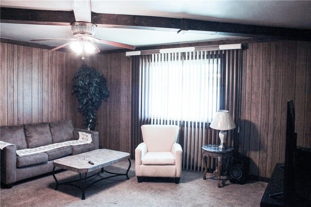 carpeted living room featuring ceiling fan, wooden walls, and beam ceiling