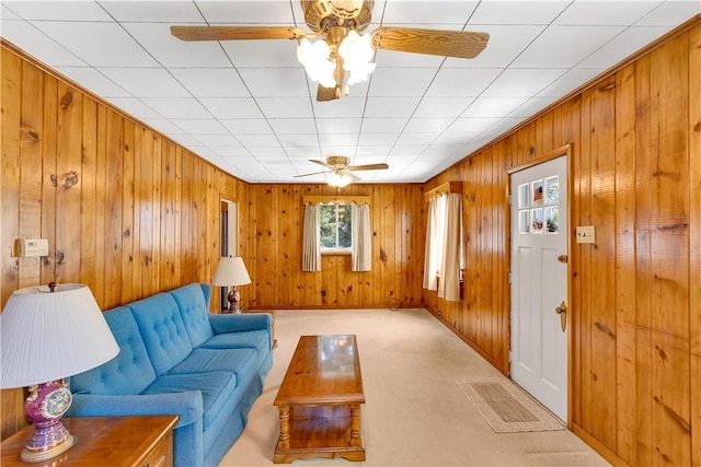 living area featuring light carpet, a ceiling fan, and wooden walls