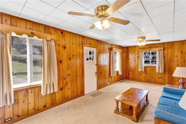 living area featuring carpet, wood walls, and ceiling fan