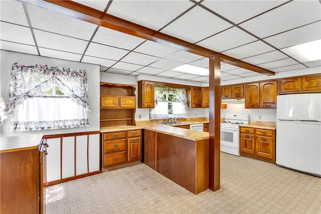 kitchen featuring a peninsula, white appliances, brown cabinetry, and a sink