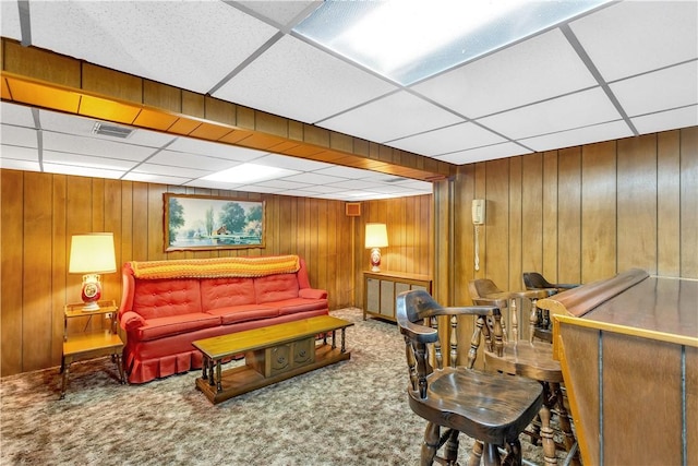 living room with a drop ceiling, carpet flooring, visible vents, and wooden walls