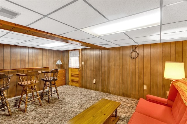 interior space with a drop ceiling, wooden walls, visible vents, a bar, and carpet