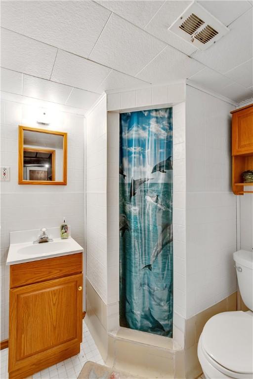 bathroom featuring toilet, vanity, visible vents, tile walls, and a stall shower