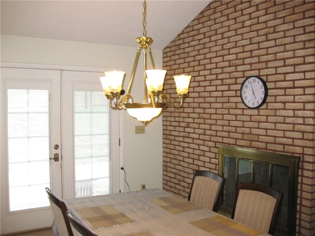 dining space featuring vaulted ceiling, a healthy amount of sunlight, brick wall, and an inviting chandelier