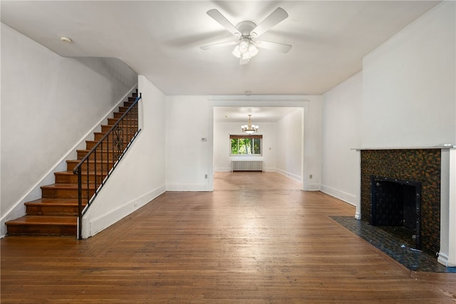 unfurnished living room with a tile fireplace, radiator heating unit, stairway, wood finished floors, and ceiling fan with notable chandelier