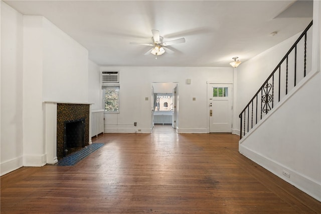 unfurnished living room with radiator heating unit, a fireplace with flush hearth, ceiling fan, wood finished floors, and stairs