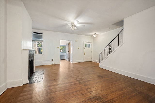 unfurnished living room with hardwood / wood-style flooring, ceiling fan, stairs, an AC wall unit, and a fireplace