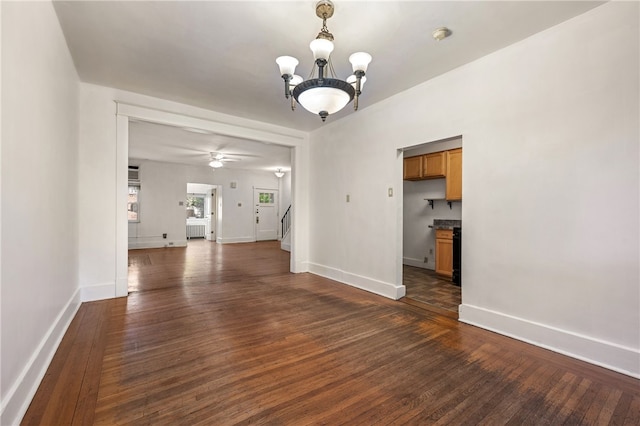 unfurnished dining area with ceiling fan with notable chandelier, dark wood-type flooring, stairway, and baseboards