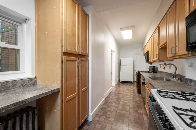 kitchen featuring brick floor, radiator, a sink, black appliances, and baseboards