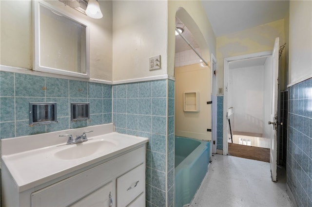 full bath featuring a wainscoted wall, tile walls, vanity, and a bath