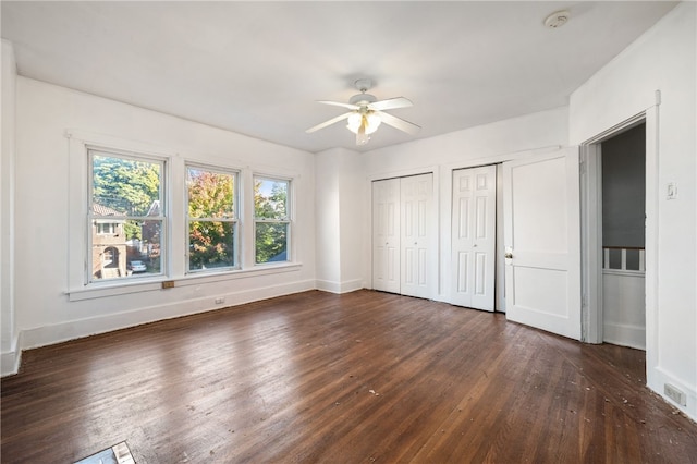 unfurnished bedroom with wood finished floors, ceiling fan, baseboards, and two closets