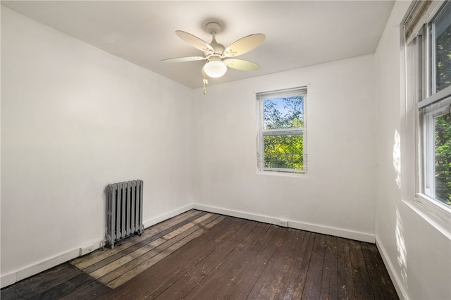 spare room featuring dark wood-style floors, baseboards, a ceiling fan, and radiator