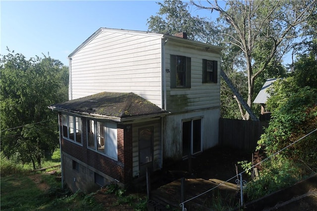 view of side of home featuring brick siding, fence, and a chimney