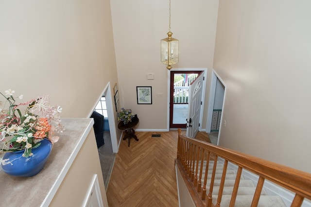 entryway featuring parquet flooring, a notable chandelier, plenty of natural light, and a high ceiling