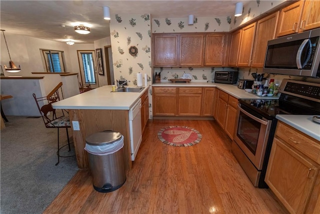 kitchen with stainless steel appliances, a breakfast bar, a sink, light wood-style flooring, and a peninsula