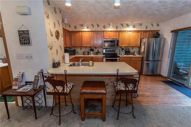 kitchen with a sink, a kitchen breakfast bar, brown cabinets, and appliances with stainless steel finishes