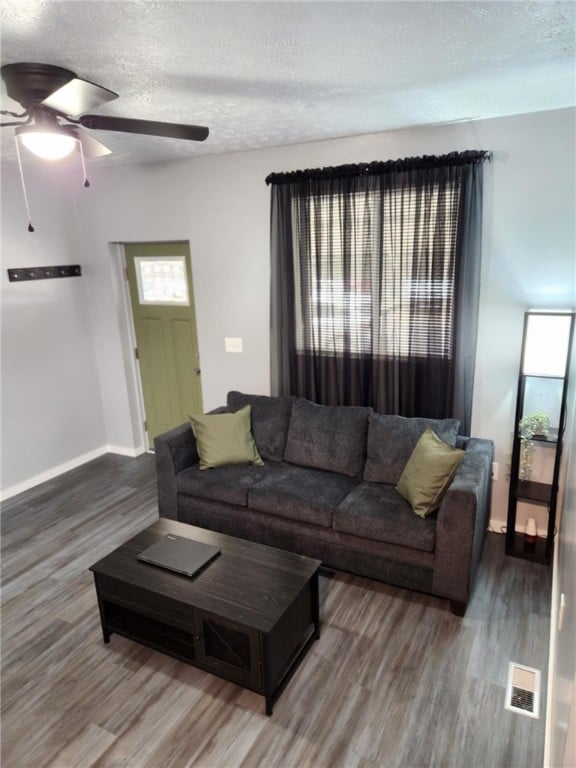 living room featuring dark wood-type flooring, ceiling fan, and a textured ceiling